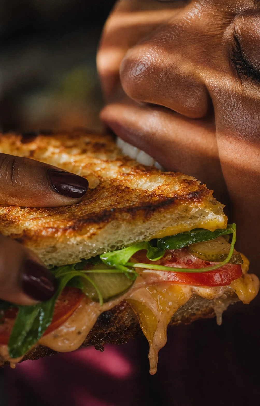A close-up of someone biting into a toasted sandwich.